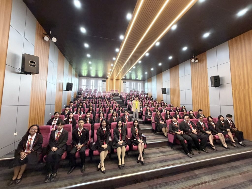 Arcinas Hall from the stage, showing the oak-slat ceiling and gold linear light strips above a seated audience.