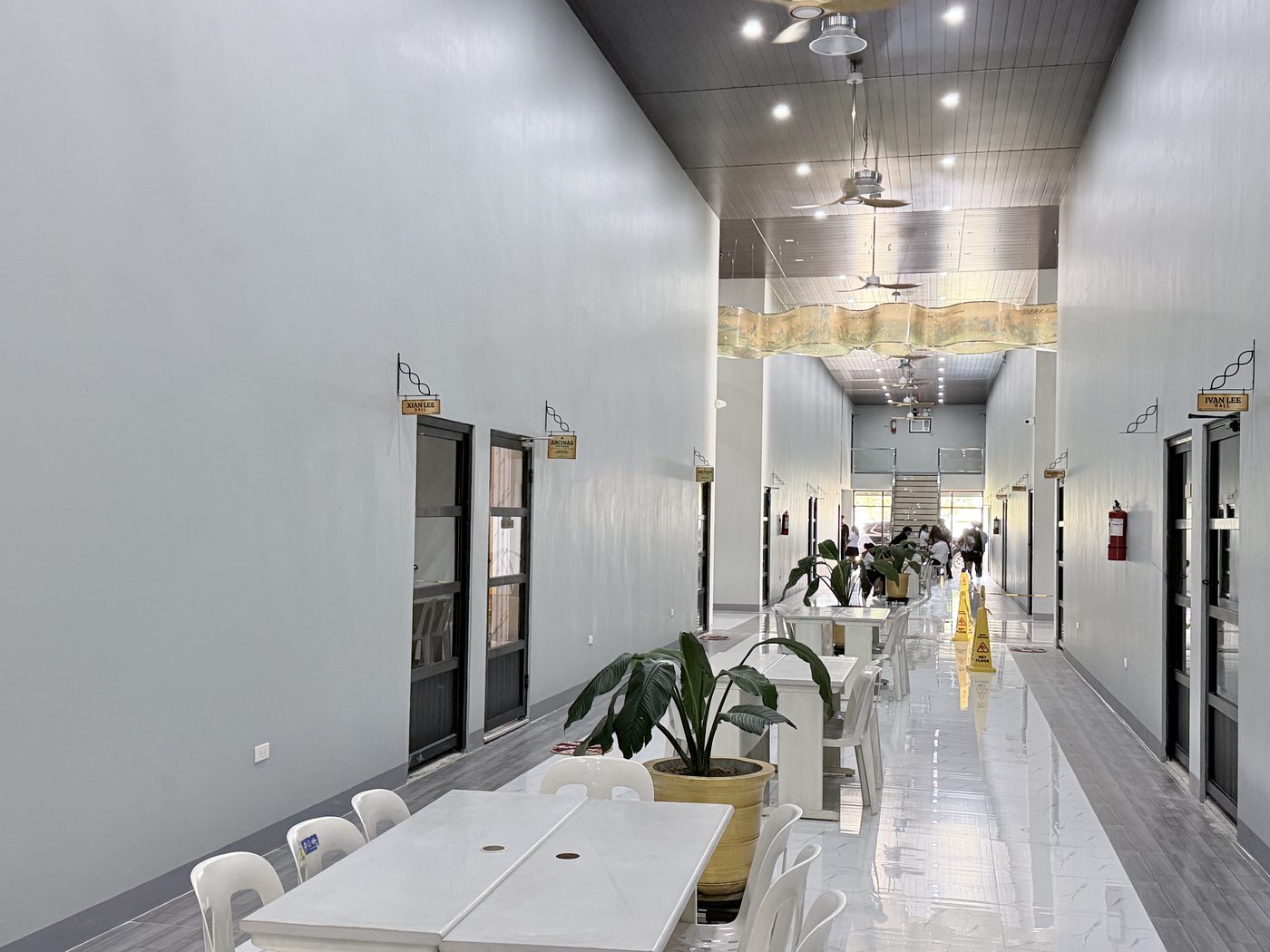 A bright interior corridor inside the main building leading toward the halls, with tiled floors and pendant lighting.