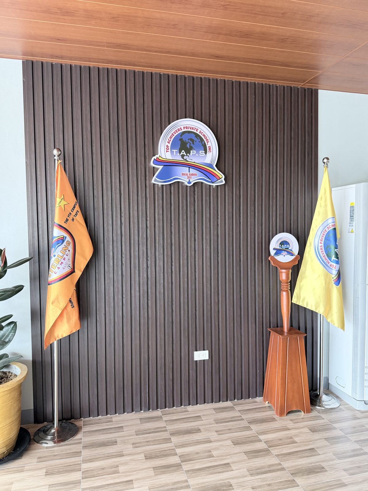 Lobby feature wall in dark timber slats with the school seal and standing flags.