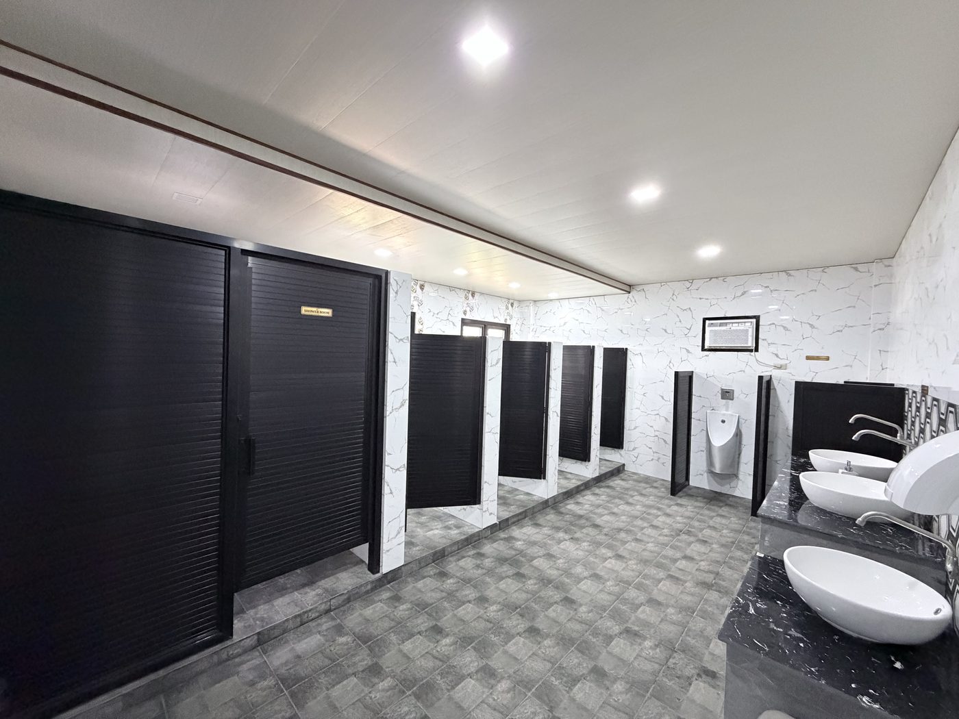 Clean tiled restroom with a row of black cubicle doors and white basins.